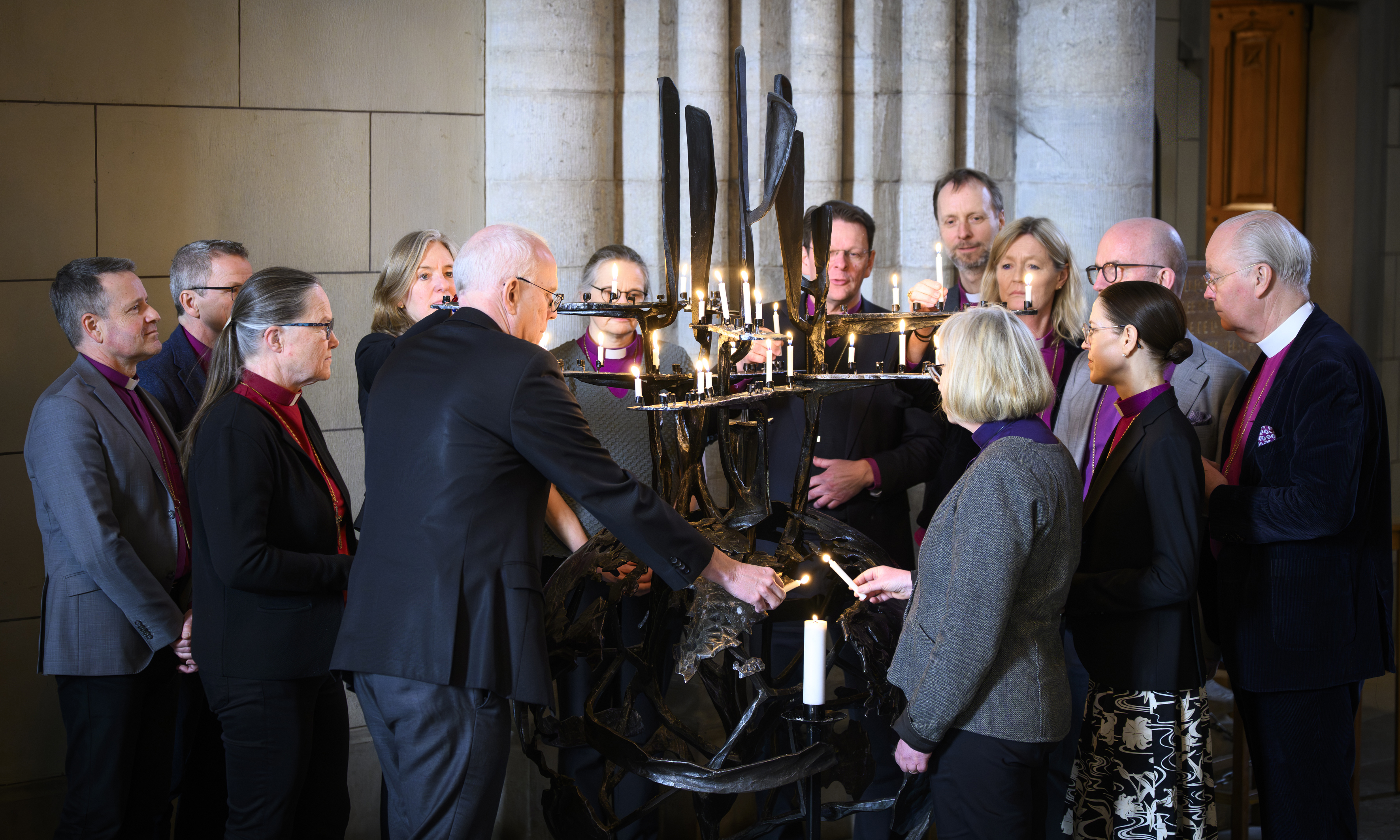 Biskoparna tänder ljus i en ljusbärare inne i kyrkan.