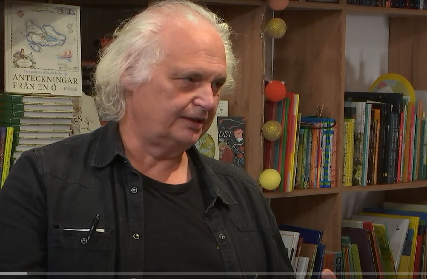 Man sitter i en bokhandel och tittar till vänster.