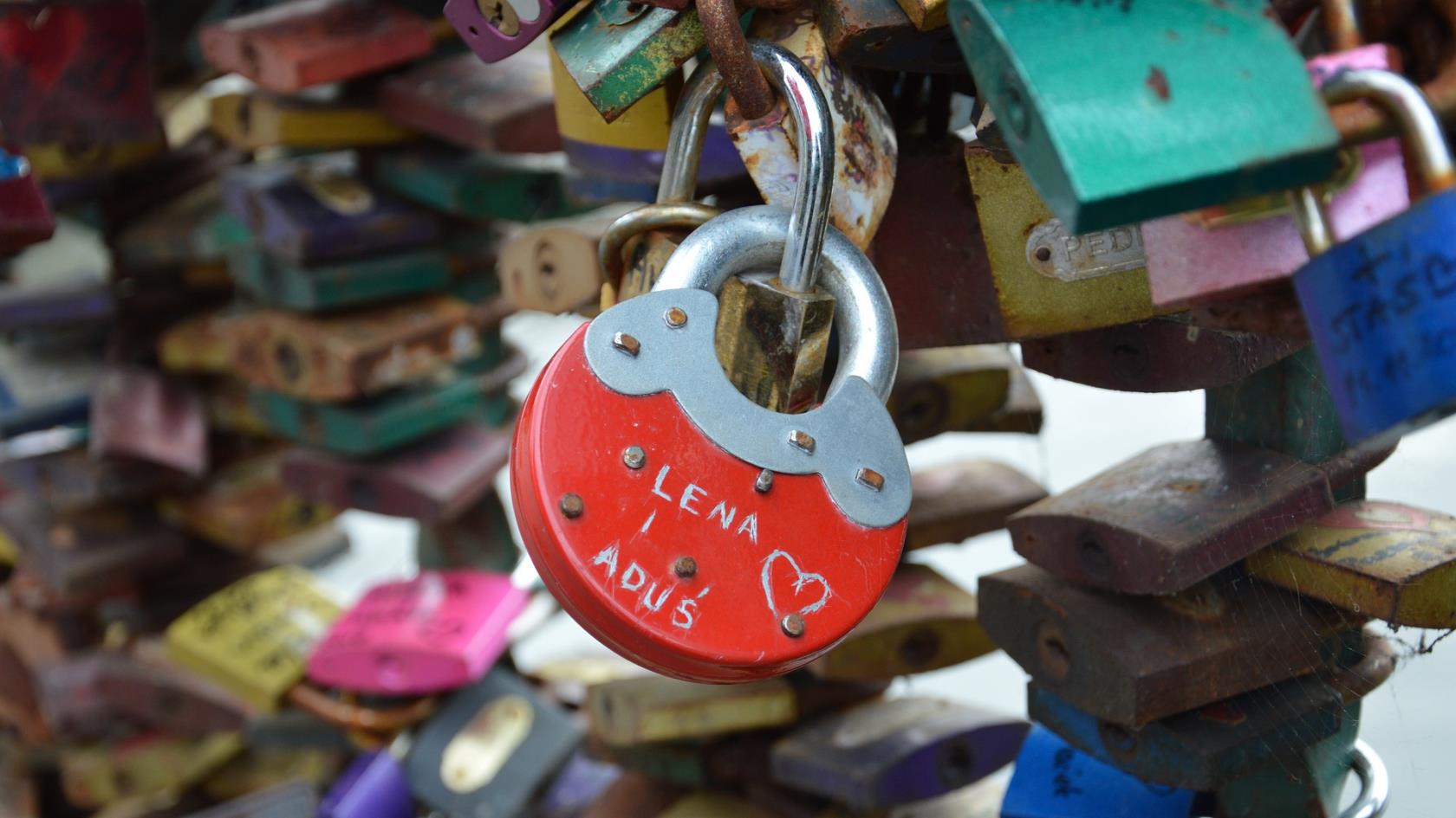 Ett rött hänglås i form av ett hjärta och två namn skrivna på låset.