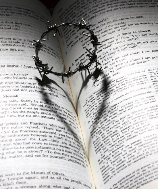 En cirkel av taggtråd lämnar en skugga i form av ett hjärta i en uppslagen bibel.
