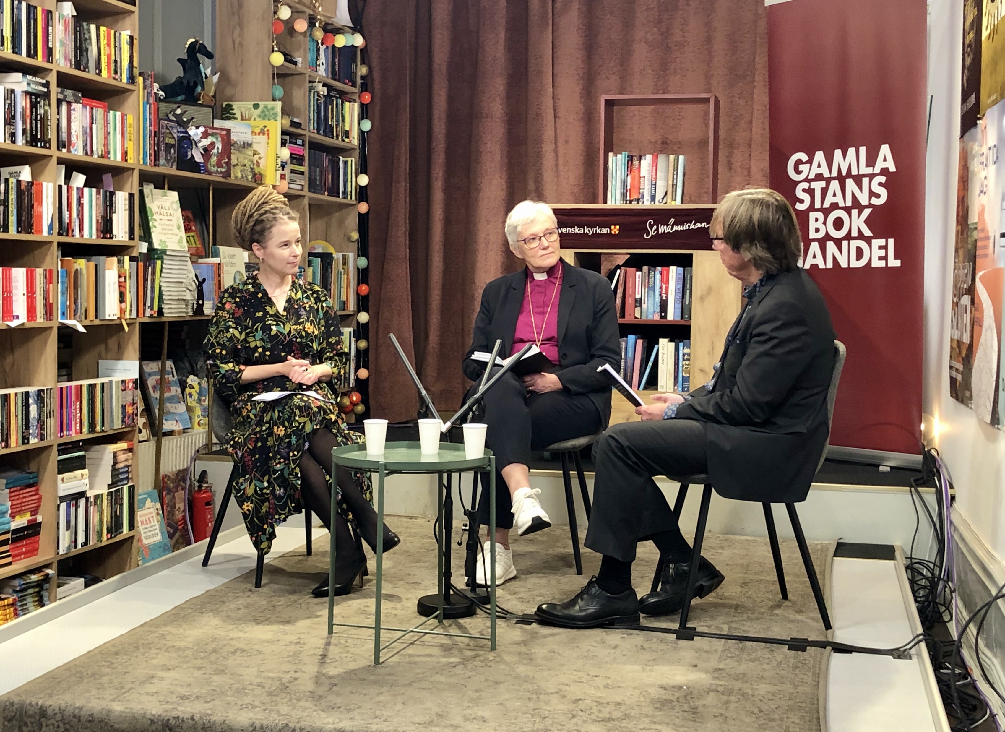Ärkebiskop Antje Jackelén sitter i Gamla stans bokhandel och samtalar med kulturminister Amanda Lind och moderator Dag Tuvelius.