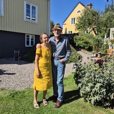 Nainen keltaisessa mekossa puutarhassa miehensä kanssa.