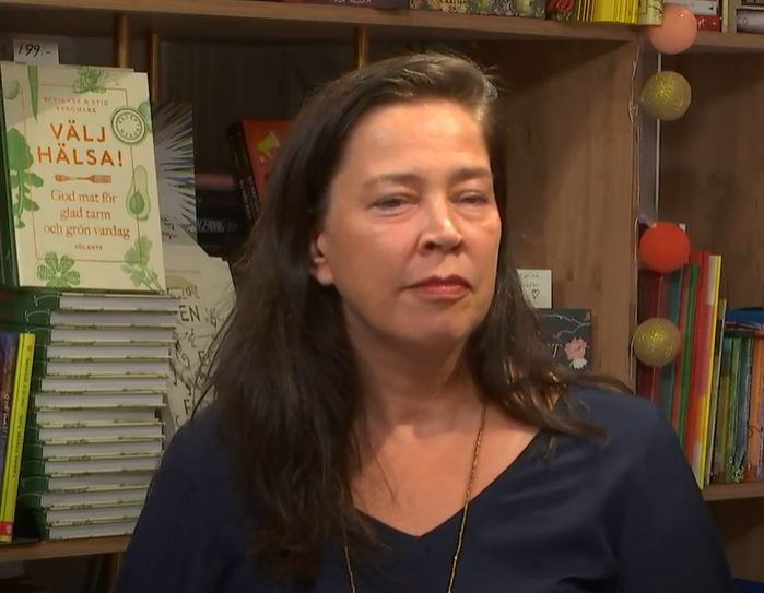 Kvinna sitter i en bokhandel med bokhylla i bakgrunden.