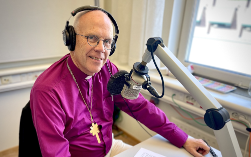 Ärkebiskop Martin Modéus sitter vid ett skrivbord med en radiomikrofon.