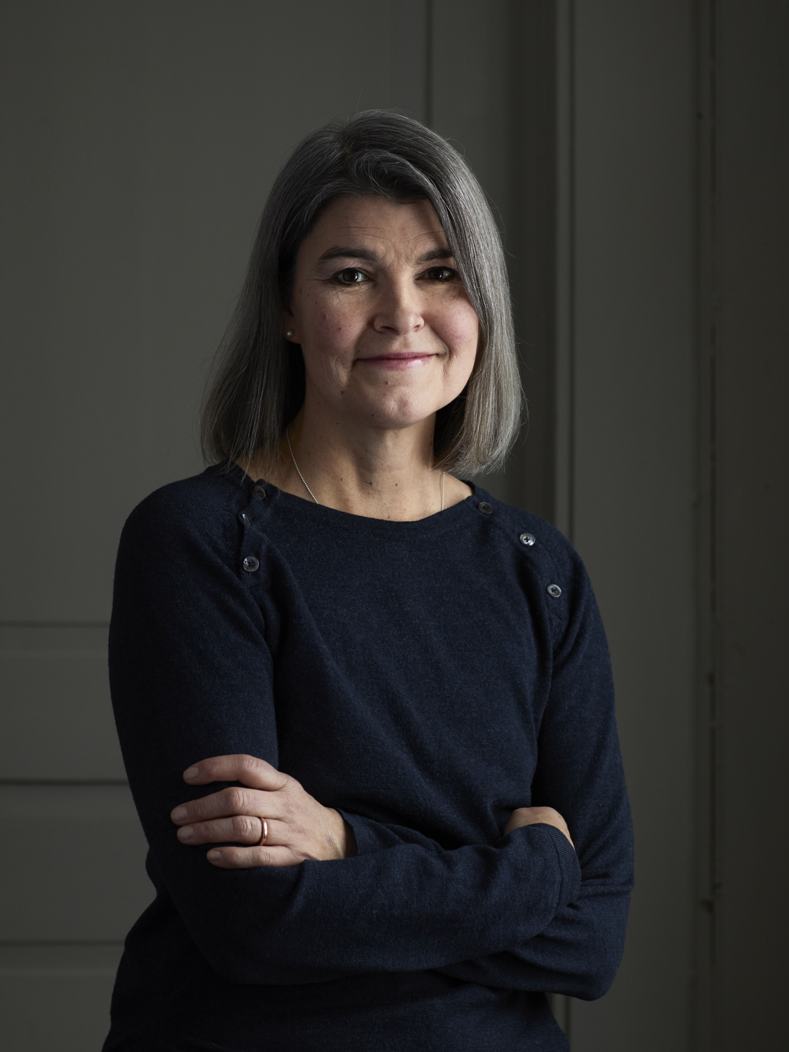 Nainen seisoo tummissa vaatteissa ja hymyilee.