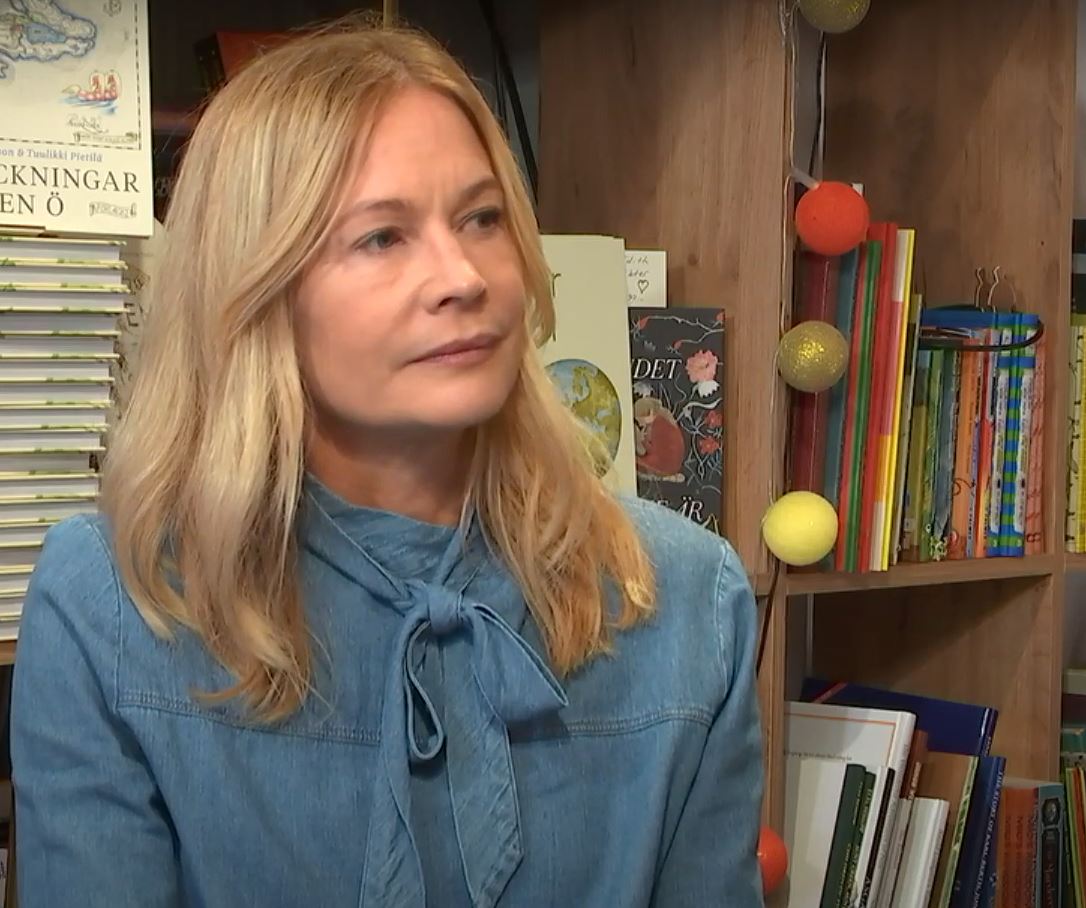 Kvinna sitter framför en bokhylla och tittar åt höger.