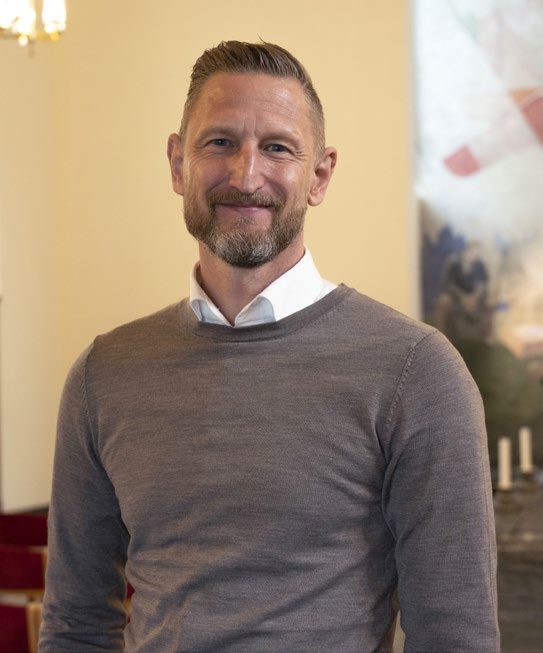 Mies katsoo kameraan ja hymyilee.