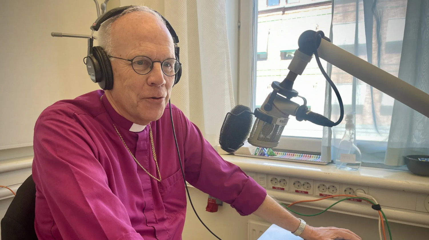Ärkebiskop Martin Modéus sitter vid ett skrivbord och pratar in i en radiomick.