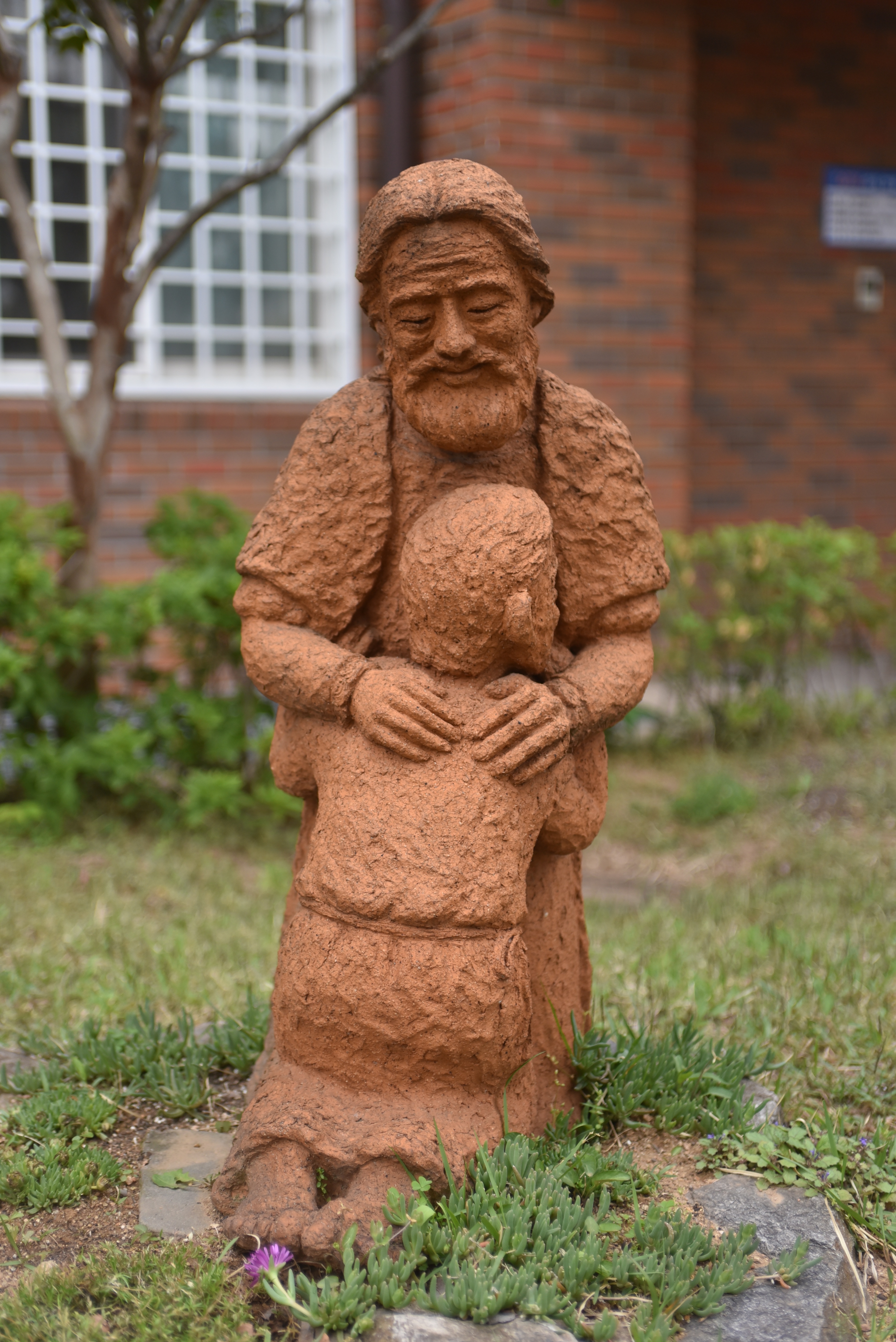Skulptur som föreställer en leende far som håller om sin knäböjande son.