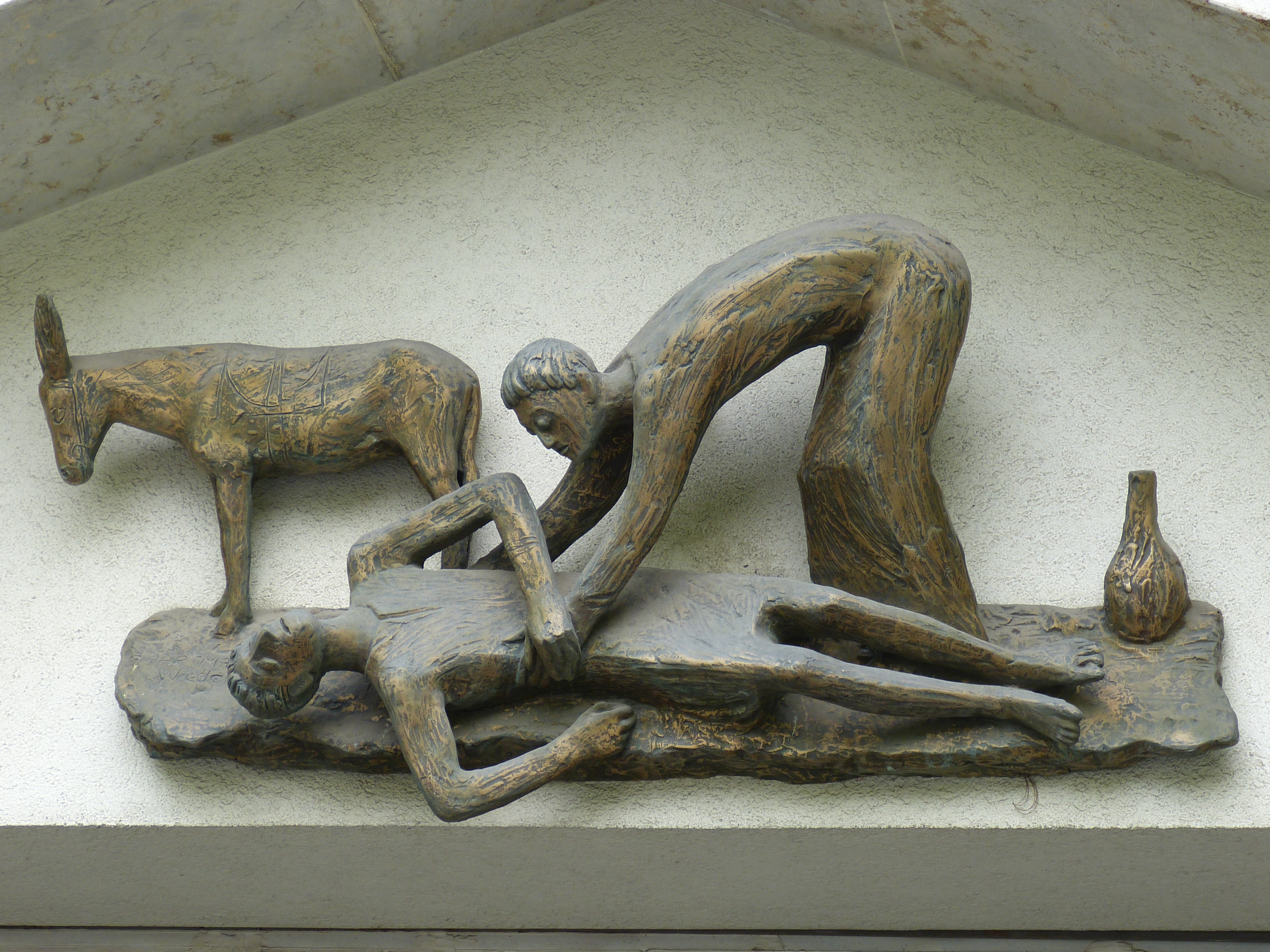 En skulptur med en liggande man och en parson som böjer sig över honom. En åsna står vid sidan.