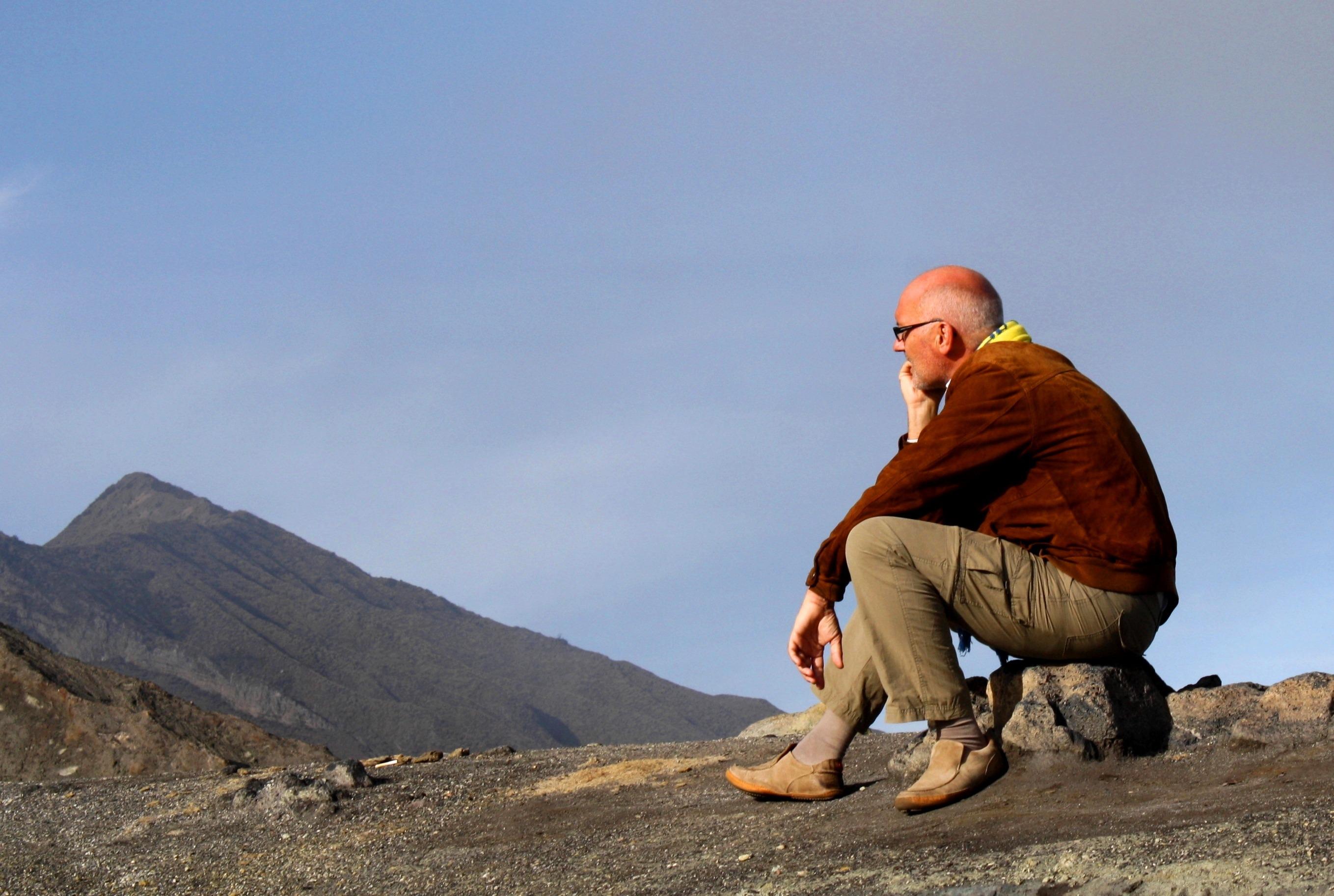 En man sitter på huk på ett berg och tänker.
