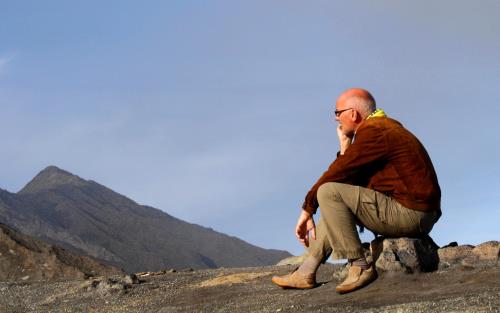 En man sitter på huk på ett berg och tänker.