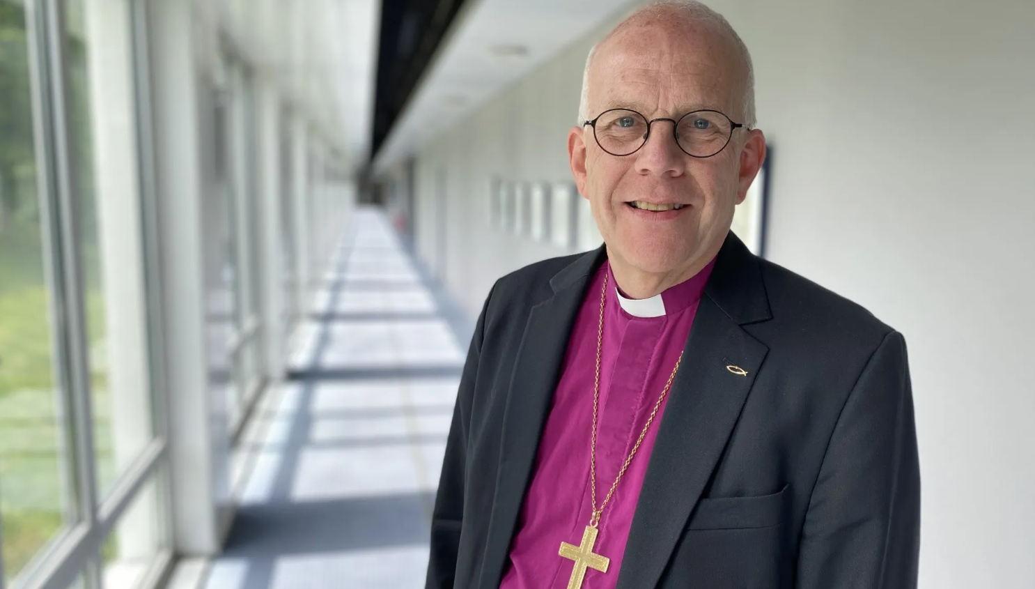 Ärkebiskop Martin Modéus ler mot kameran i lila biskopsskjorta och svart kavaj.