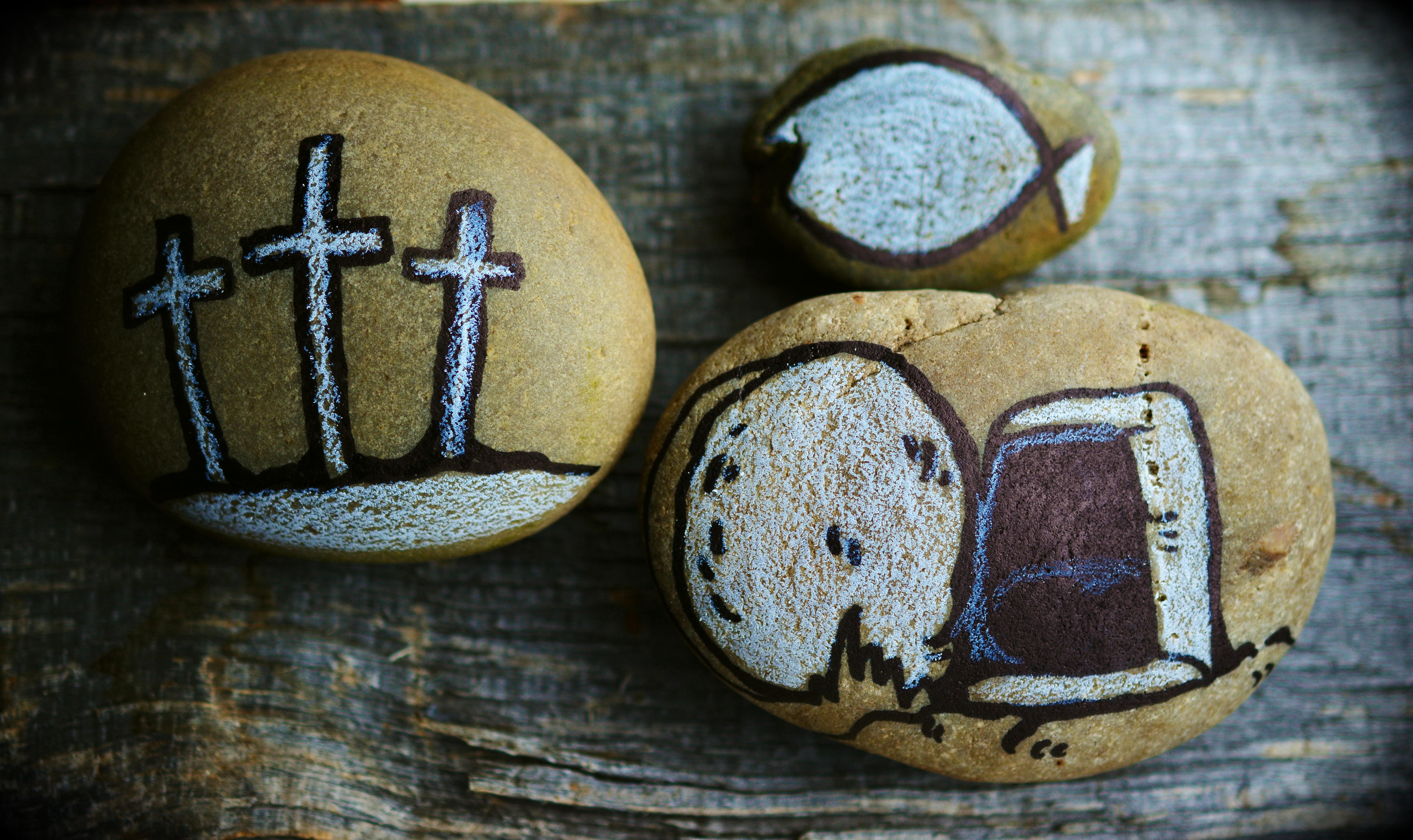 Tre målade stenar. En med tre kors, en med en fisk och en med Jesus tomma grav.