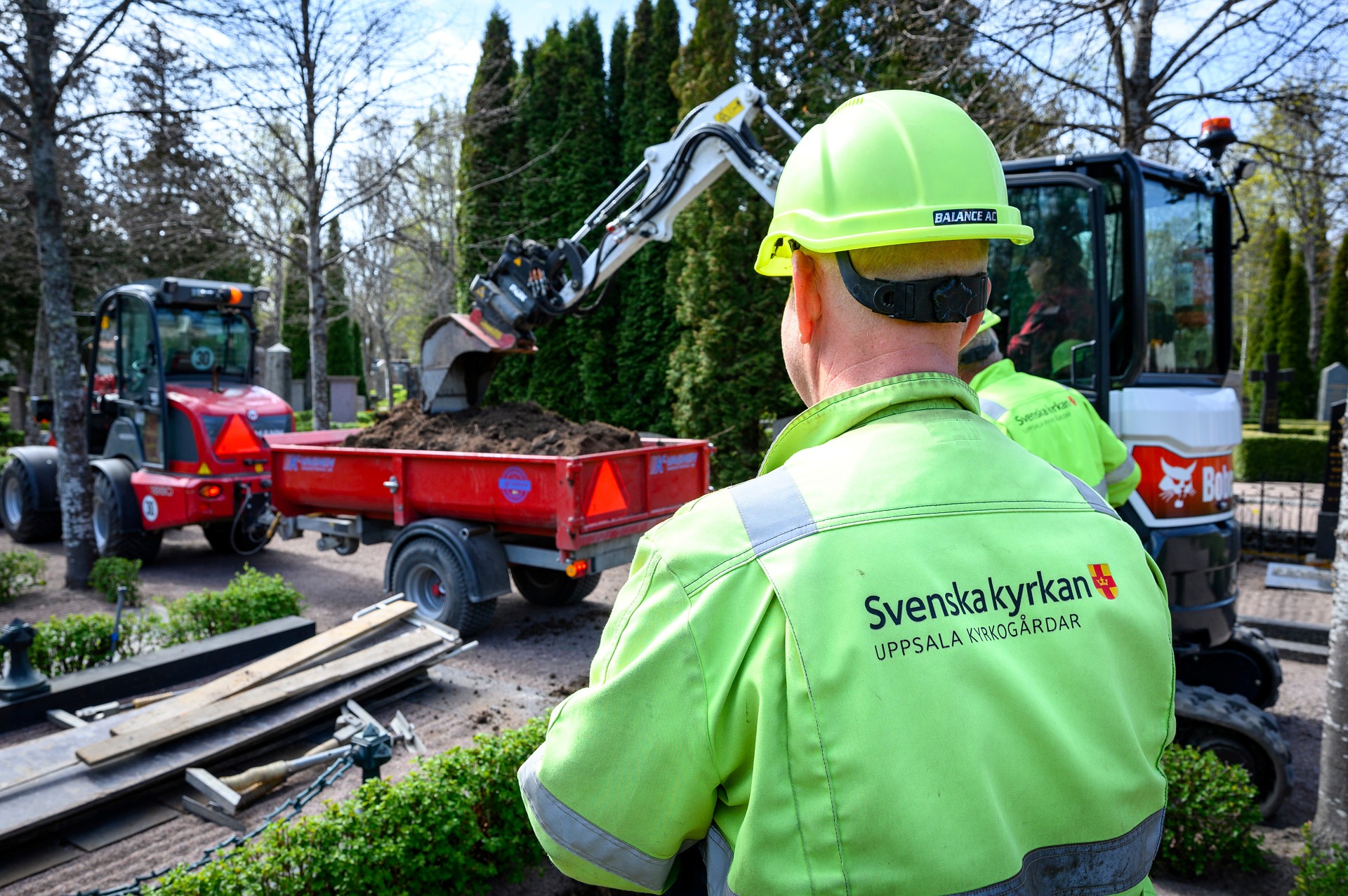 Två män som beskådar en grävmaskin på kyrkogård