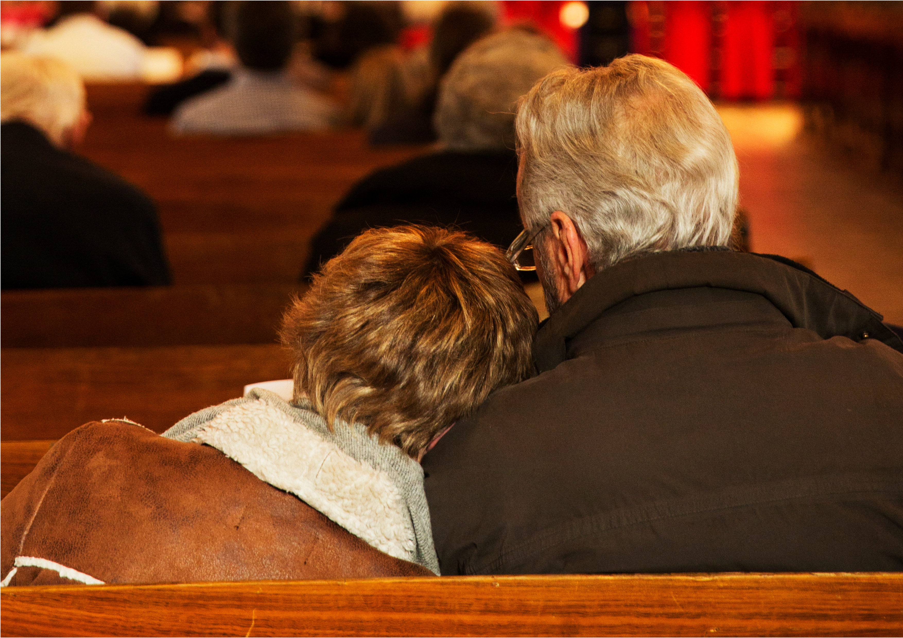 Två personer sitter i kyrkbänken med ryggen mot åskådaren.