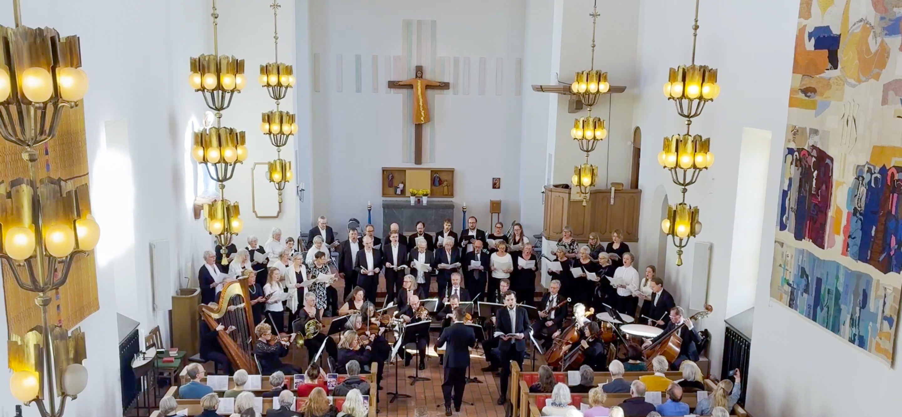 En stor kör som står längst fram i kyrkans kor, tillsammans med musiker med olika instrument.