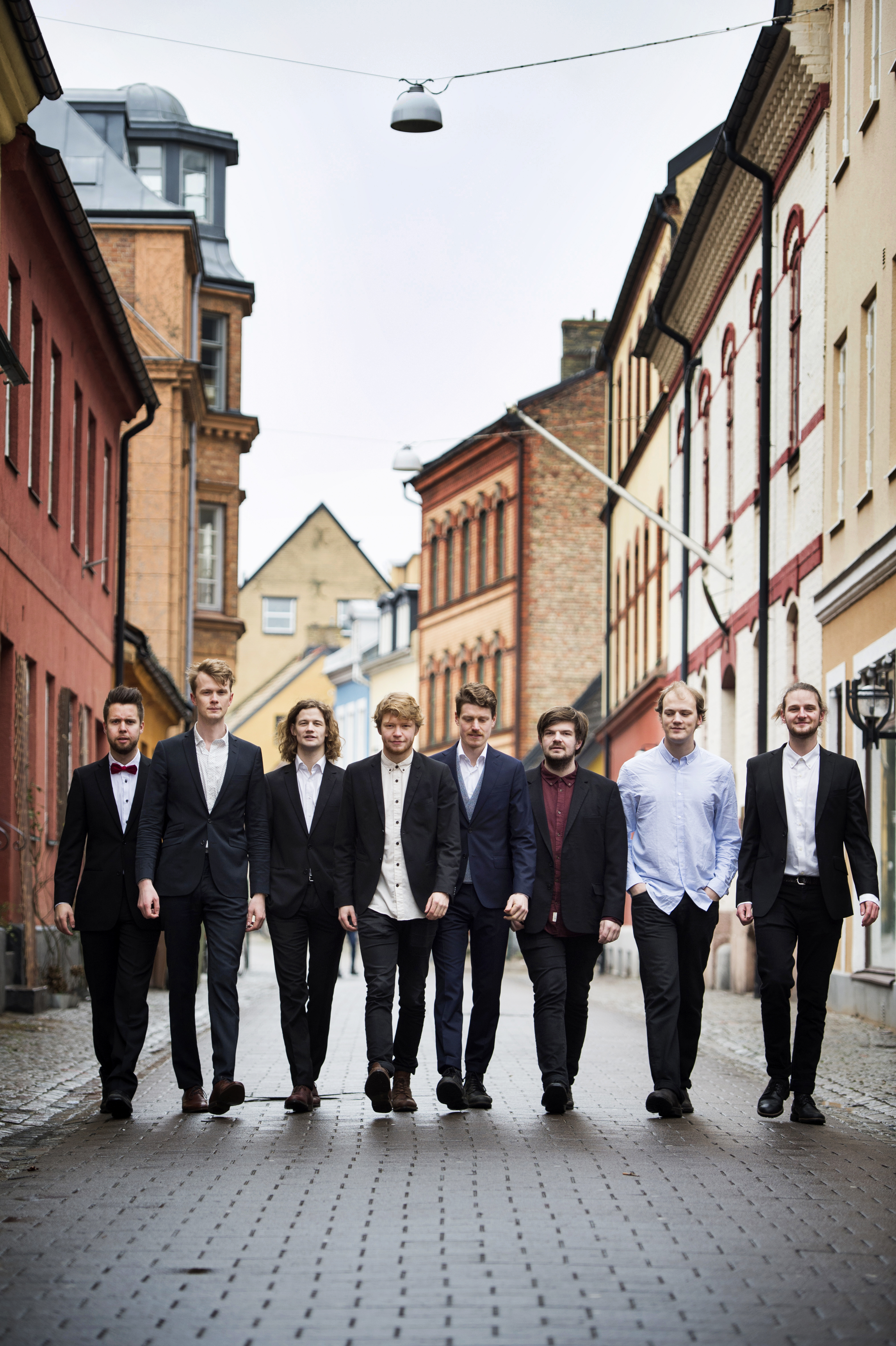 Åtta män som går på kullerstensgata med hus på var sida