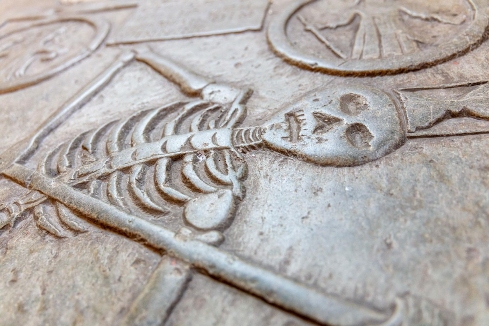 Närbild på en gravsten i golvet smyckad med en bild av ett skelelett som ser ut som en lieman.