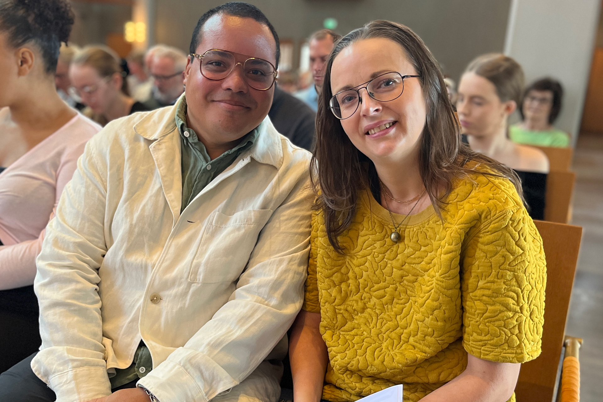 En lätt färgad man med glasögon i grön skjorta och ljus kavaj tillsammans med en kvinna med brunt axellångt hår och glasögon klädd i gult.