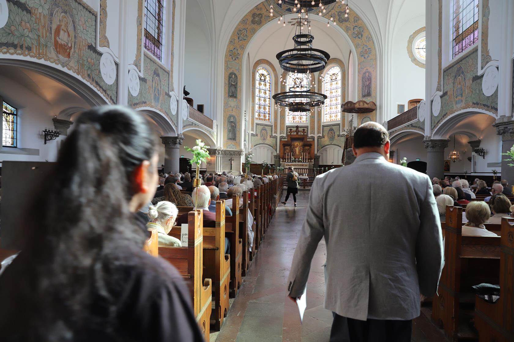 Fullsatt S:t Johannes kyrka redo för gudstjänst. Två människor går mot altaret med ryggen mot kameran.