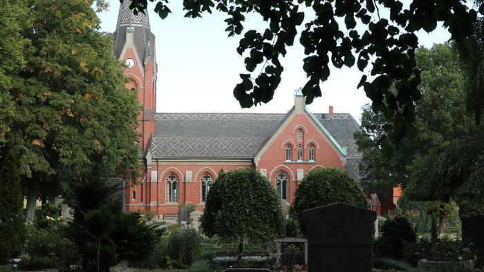 Limhamns kyrka sedd från kyrkogården med träd och buskar i förgrunden.