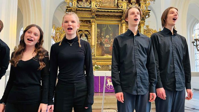 Fokus på fyra ungdomar klädda i svart som sjunger framför altare.