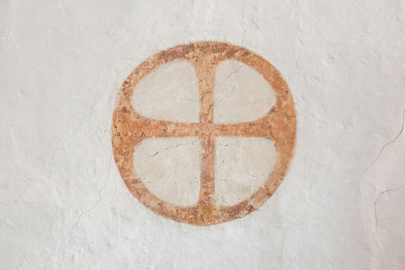 Brunrött kors i en brunröd cirkel målat på en vit vägg.