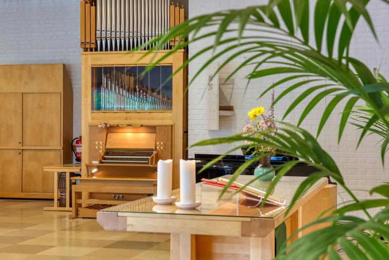 Liten orgel i trä med synliga pipor. I förgrunden ett palmblad och ett altarbord med ljus och blommor.
