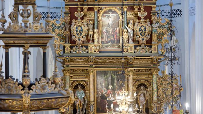 Överdådigt utsmyckad altartavla i guldiga toner och tre centrala oljemålningar.