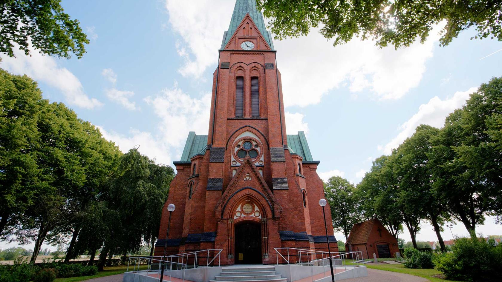 Röd tegelkyrka omgiven av träd.