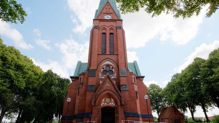 Röd tegelkyrka omgiven av träd.