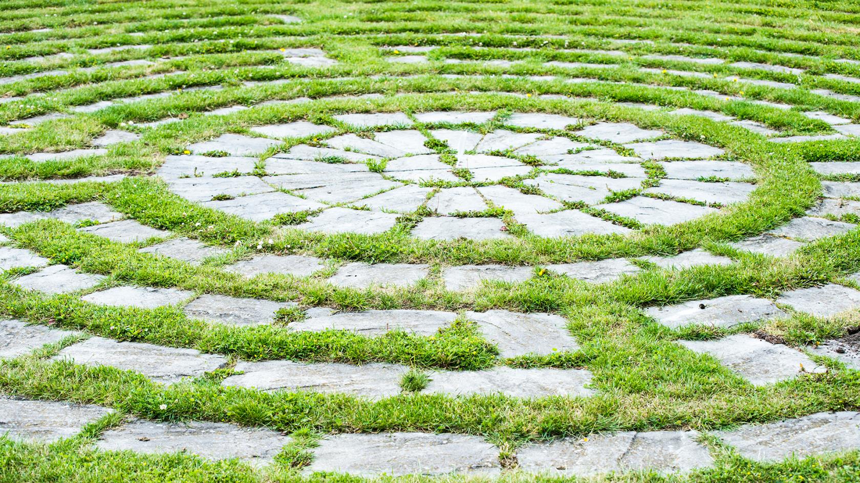 Grå betongplattor i gräsmattan i form av en labyrint med labyrintens centrum.