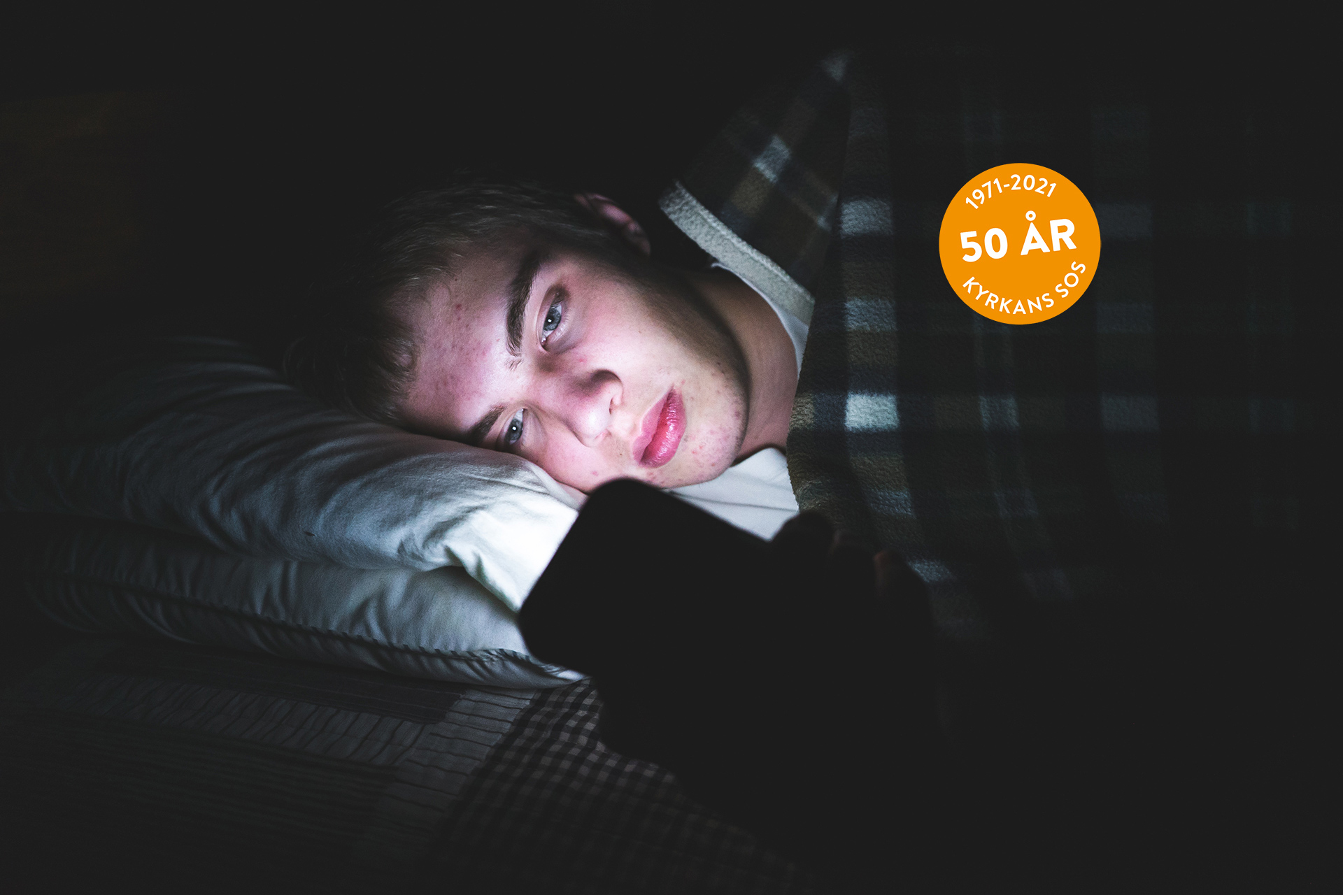 Ung kille ligger i mörkret och tittar på sin mobiltelefon.