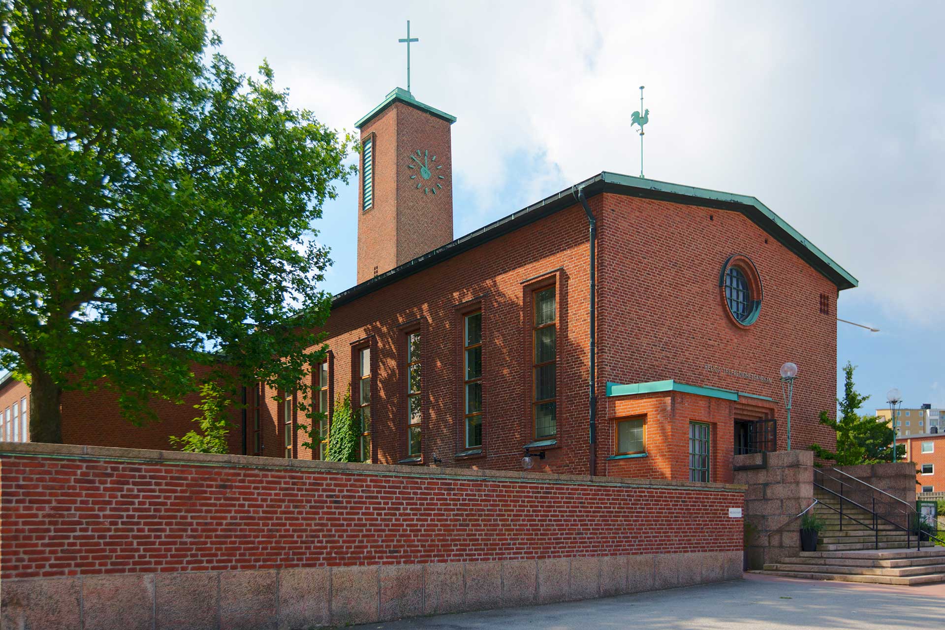 Röd tegelkyrka, tegelmur utanför och en stor bred trappa.