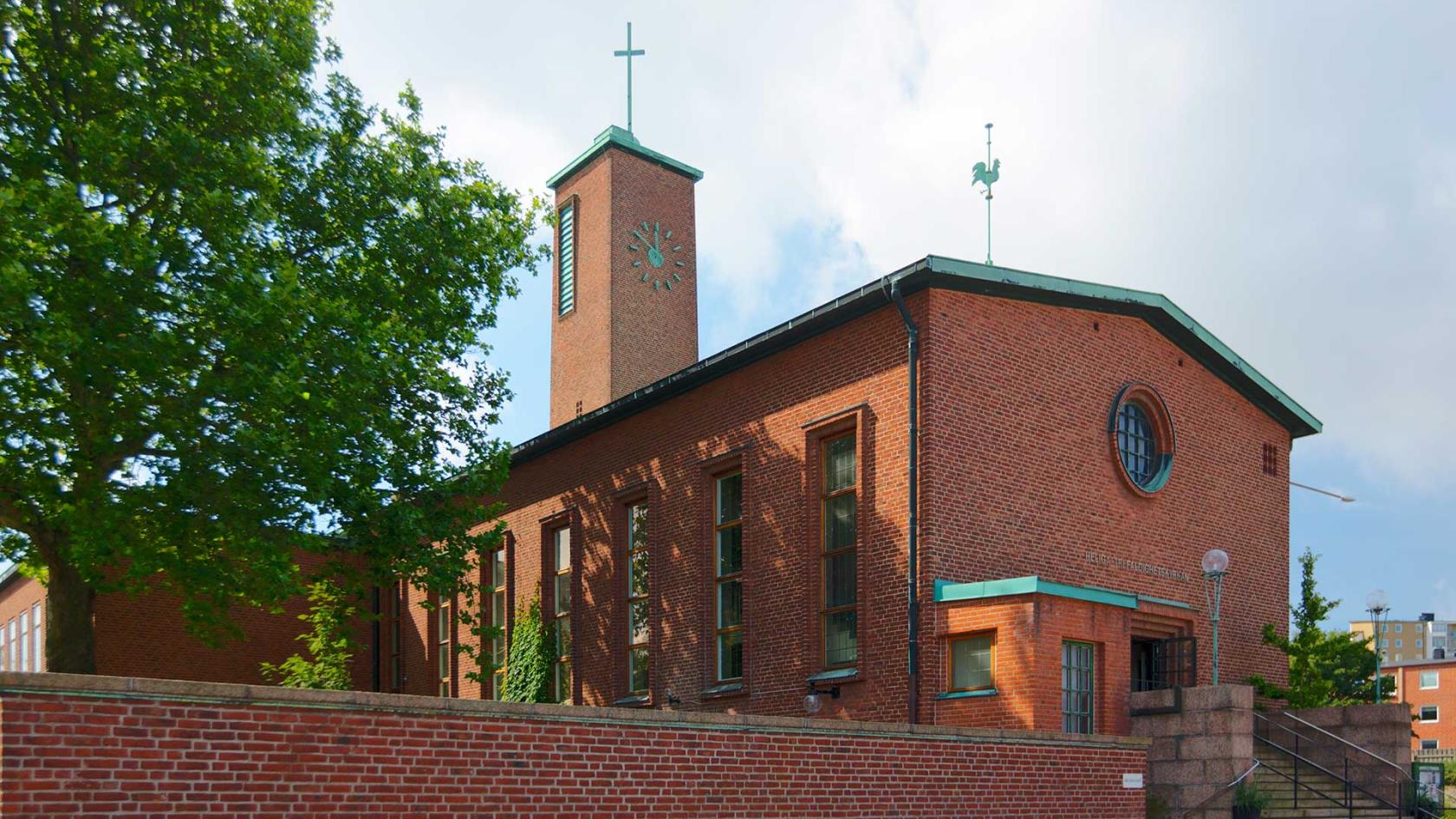 Röd tegelkyrka, tegelmur utanför och en stor bred trappa.