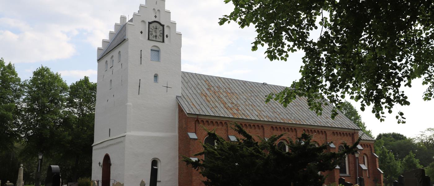 Vitt kyrktorn och ett huvudskepp i rött tegel.