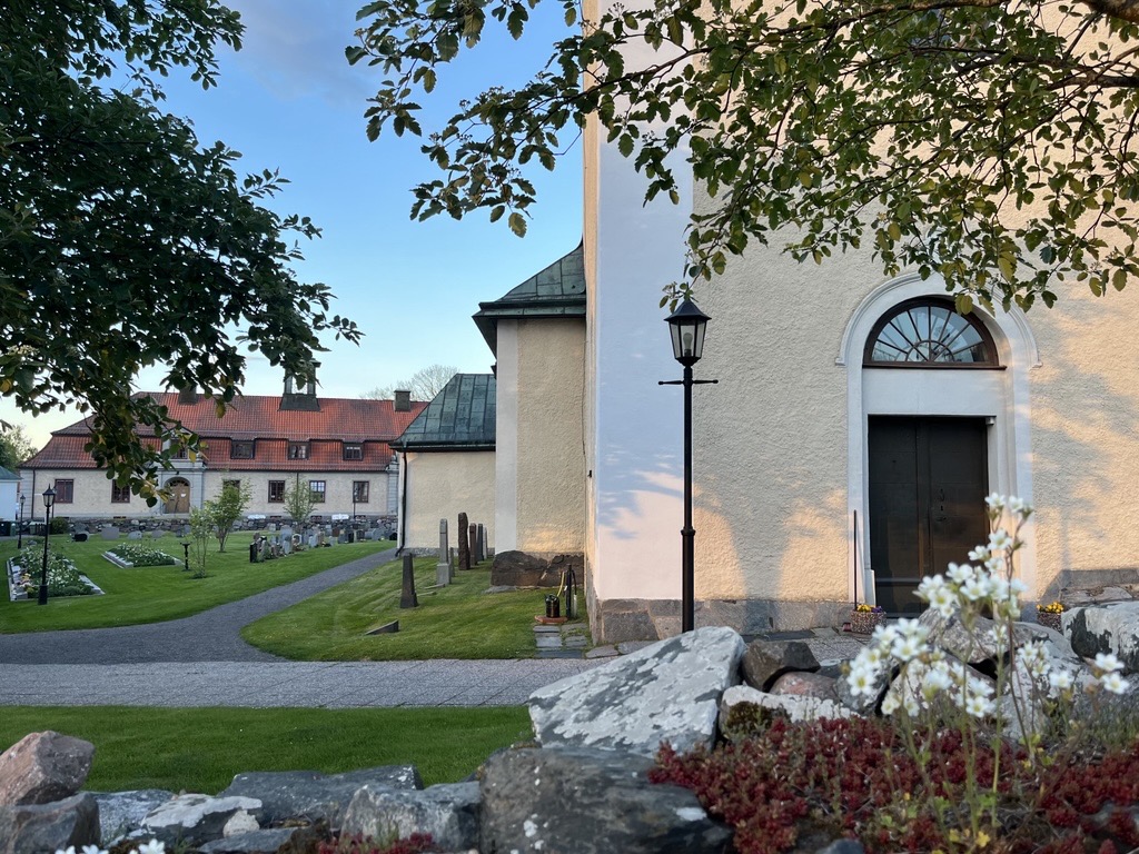 Östhammars kyrka + församlingsgård + blommor och träd i förgrunden