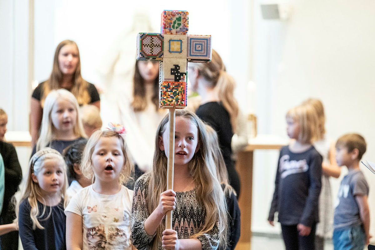 Barn som sjunger och går i procession  kyrkan, bär ett färgglatt kors.