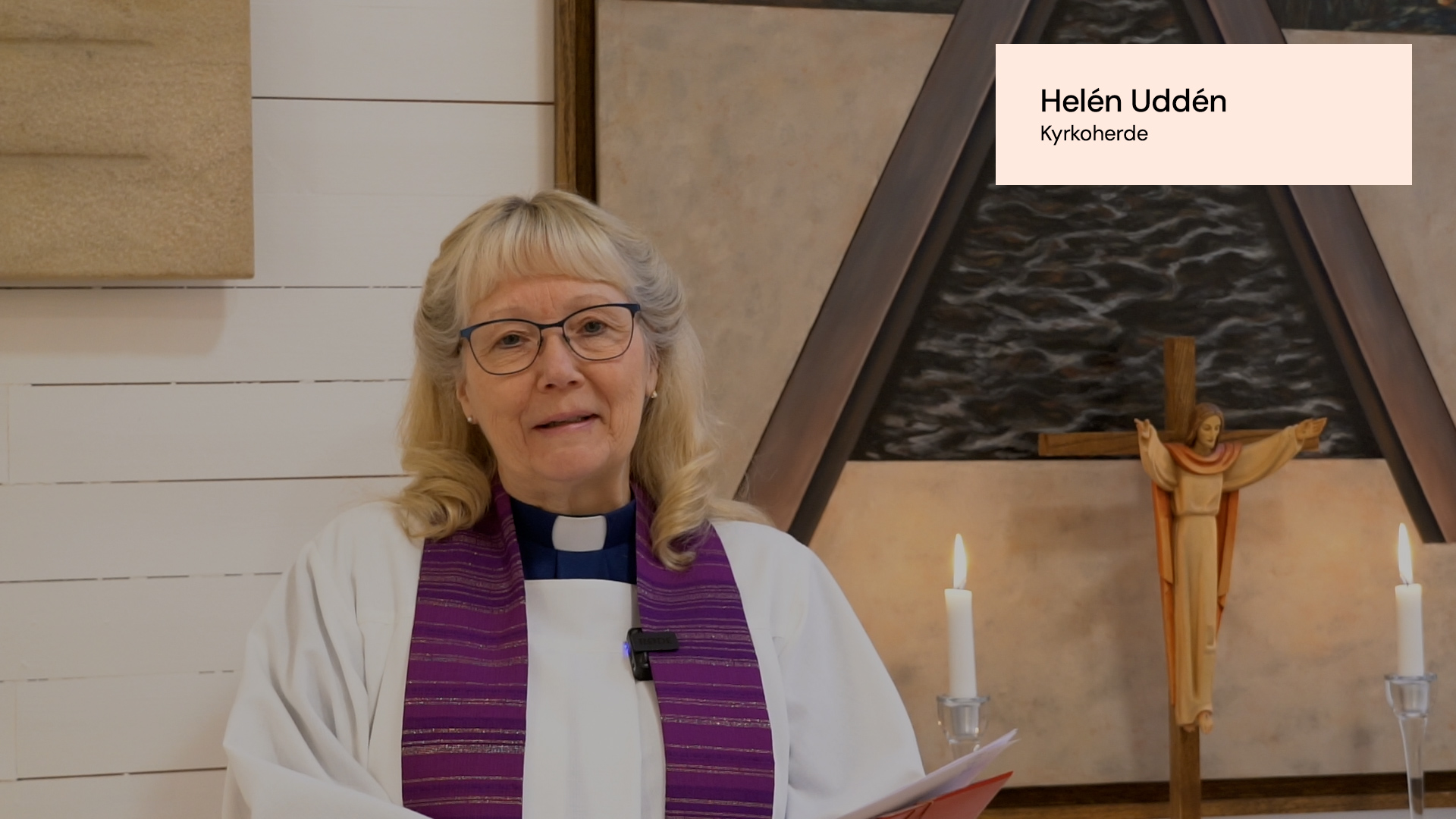 En kvinnlig präst med vit klädnad och en lilafärgad stola står framför ett altare. 