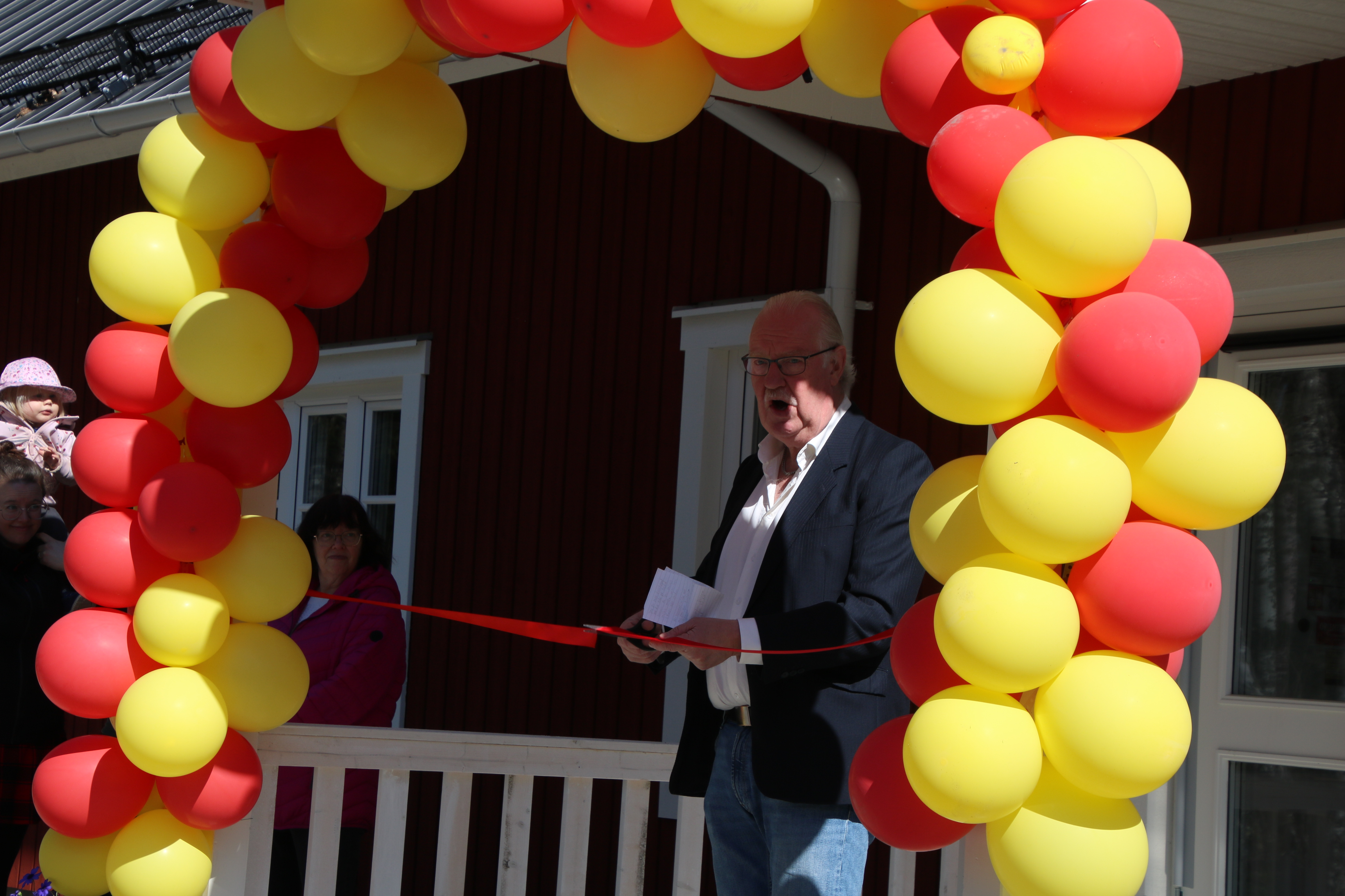 En man står med en sax och klipper av ett rött sidenband