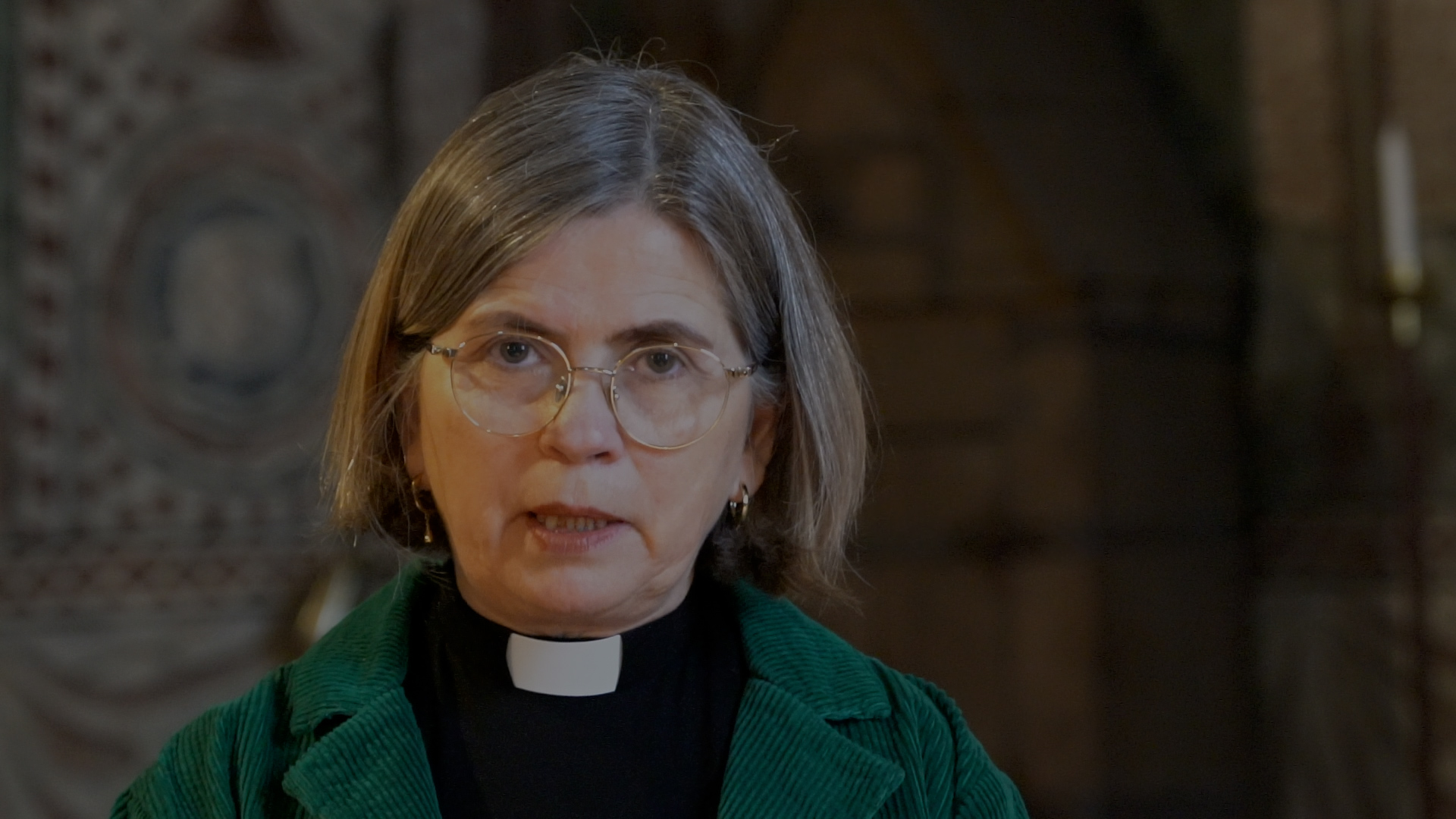 En kvinna med glasögon  i prästkrage och grön kavaj. 