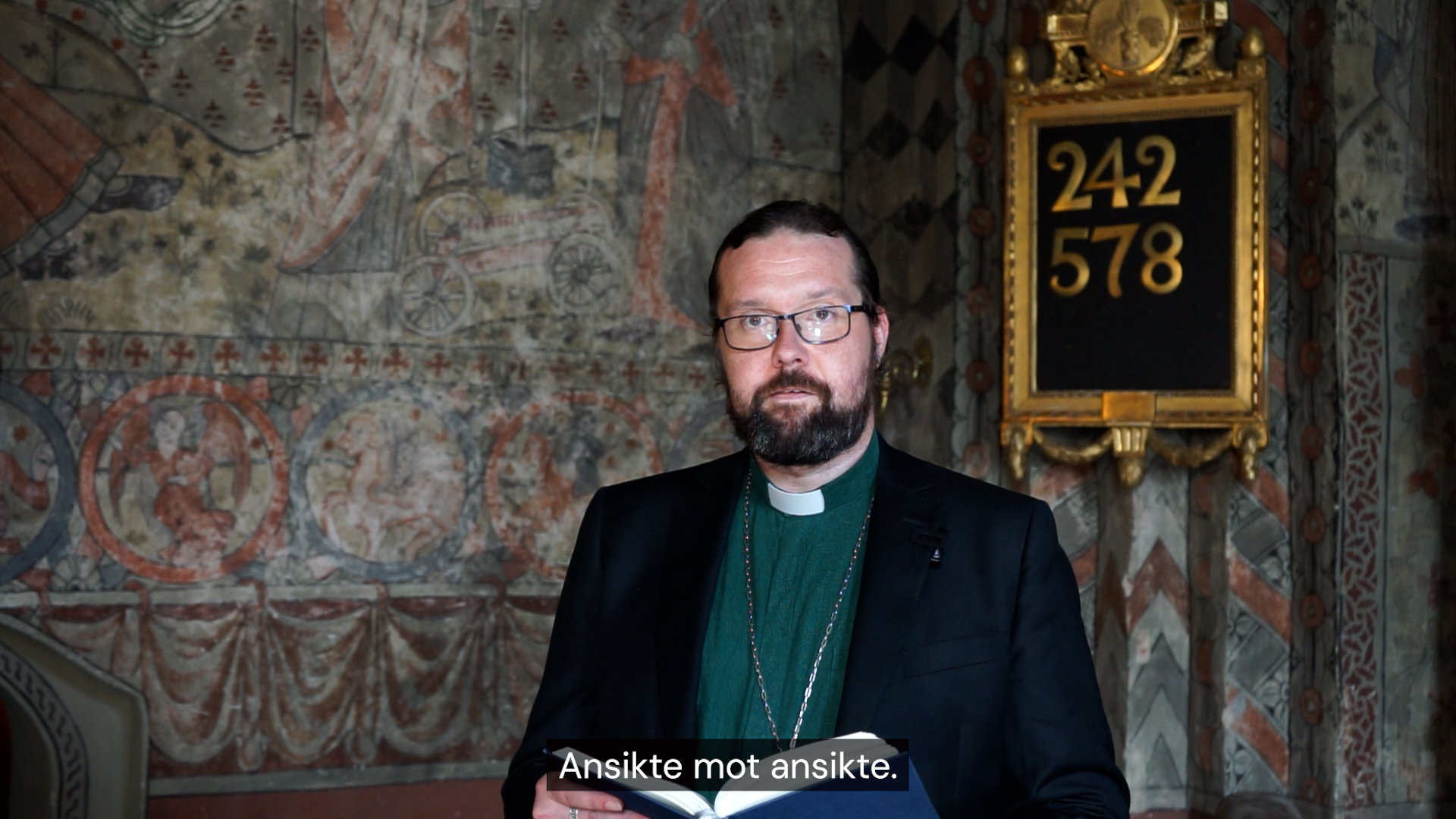 En man i skägg och glasögon har grön diakonskjorta och ett hängsmycke.