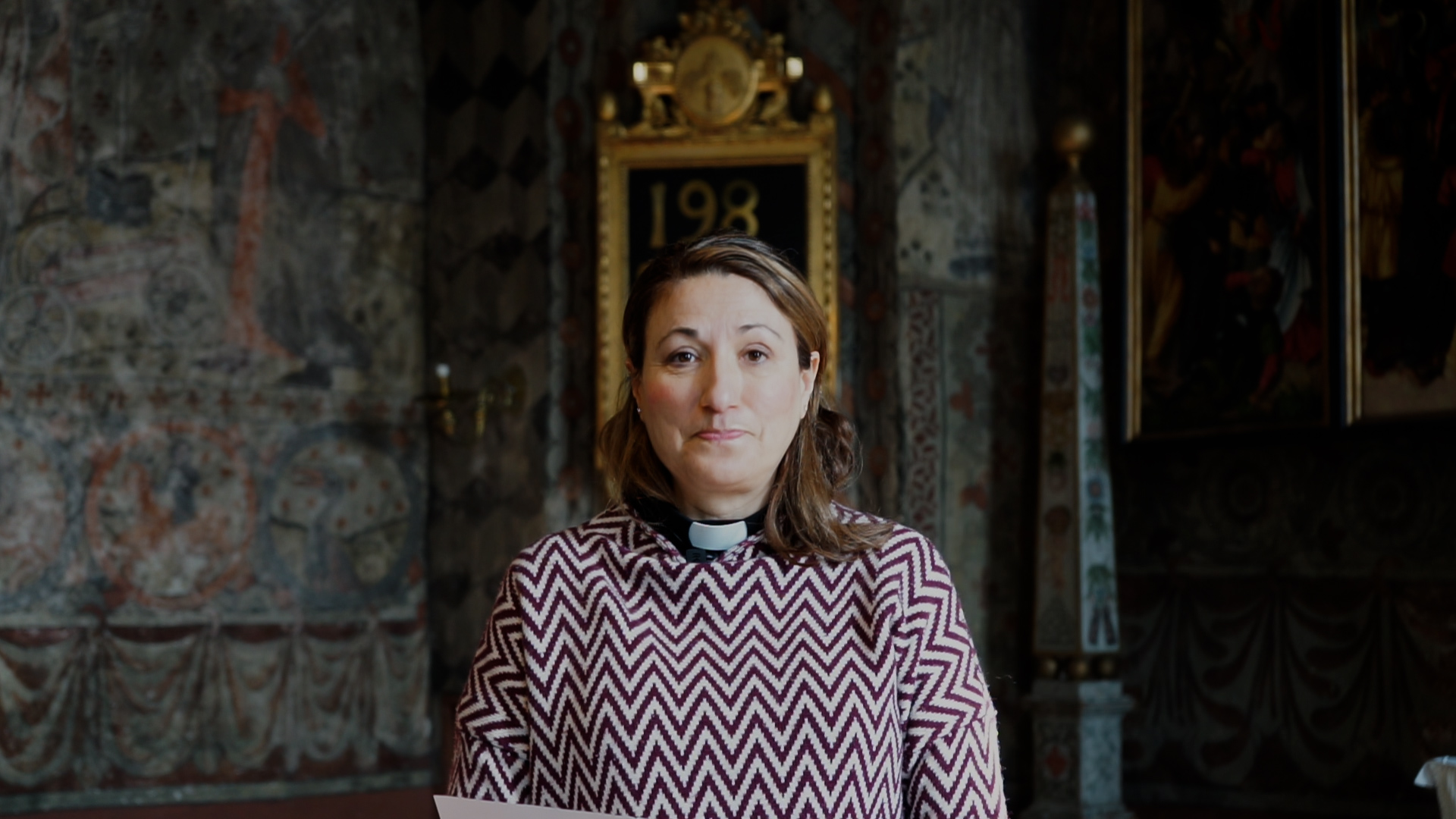 En kvinna med prästkrage står framför ett altare i en kyrka. 