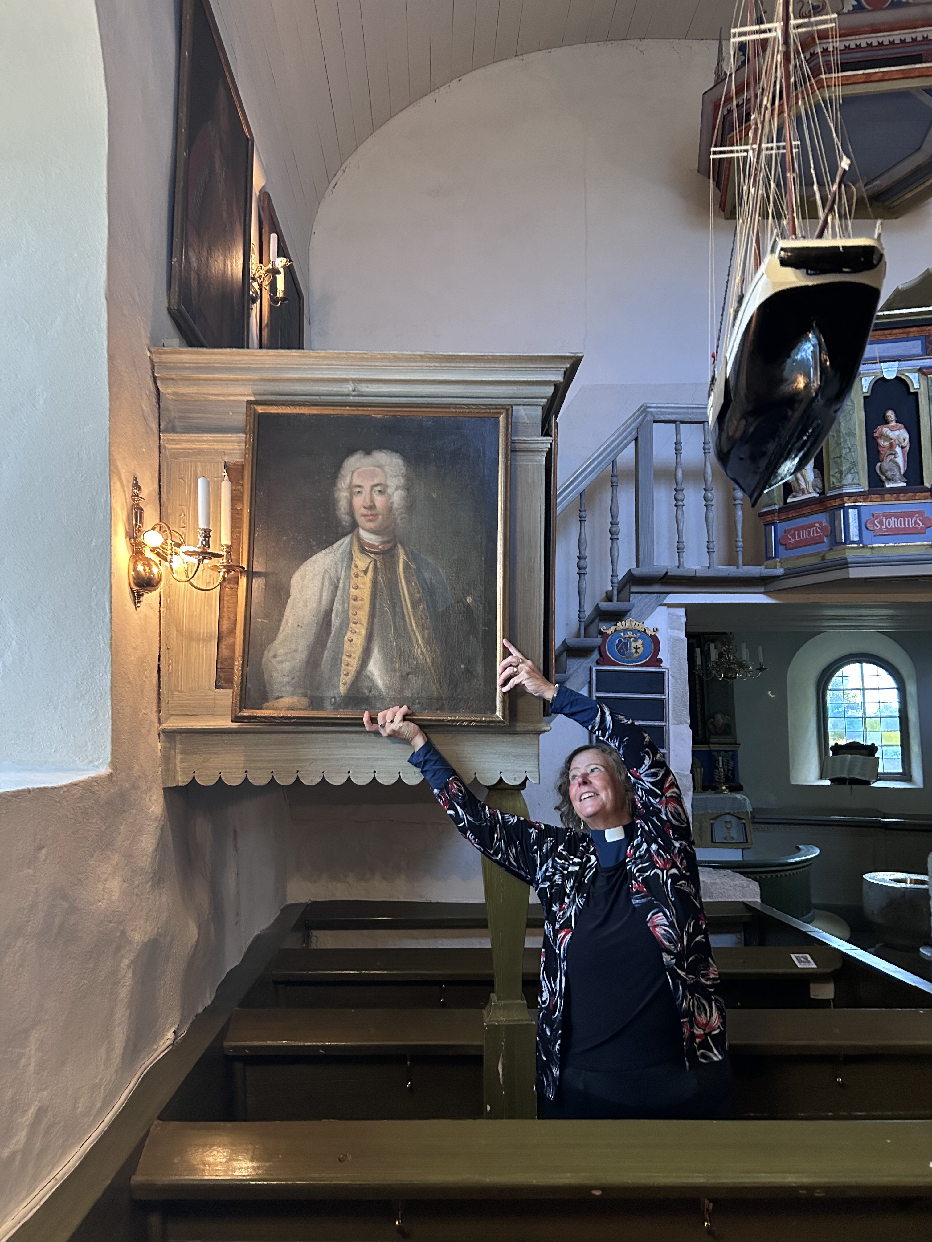 Kyrkoherde Monica håller upp tavlan på sin ursprungliga plats i kapellet