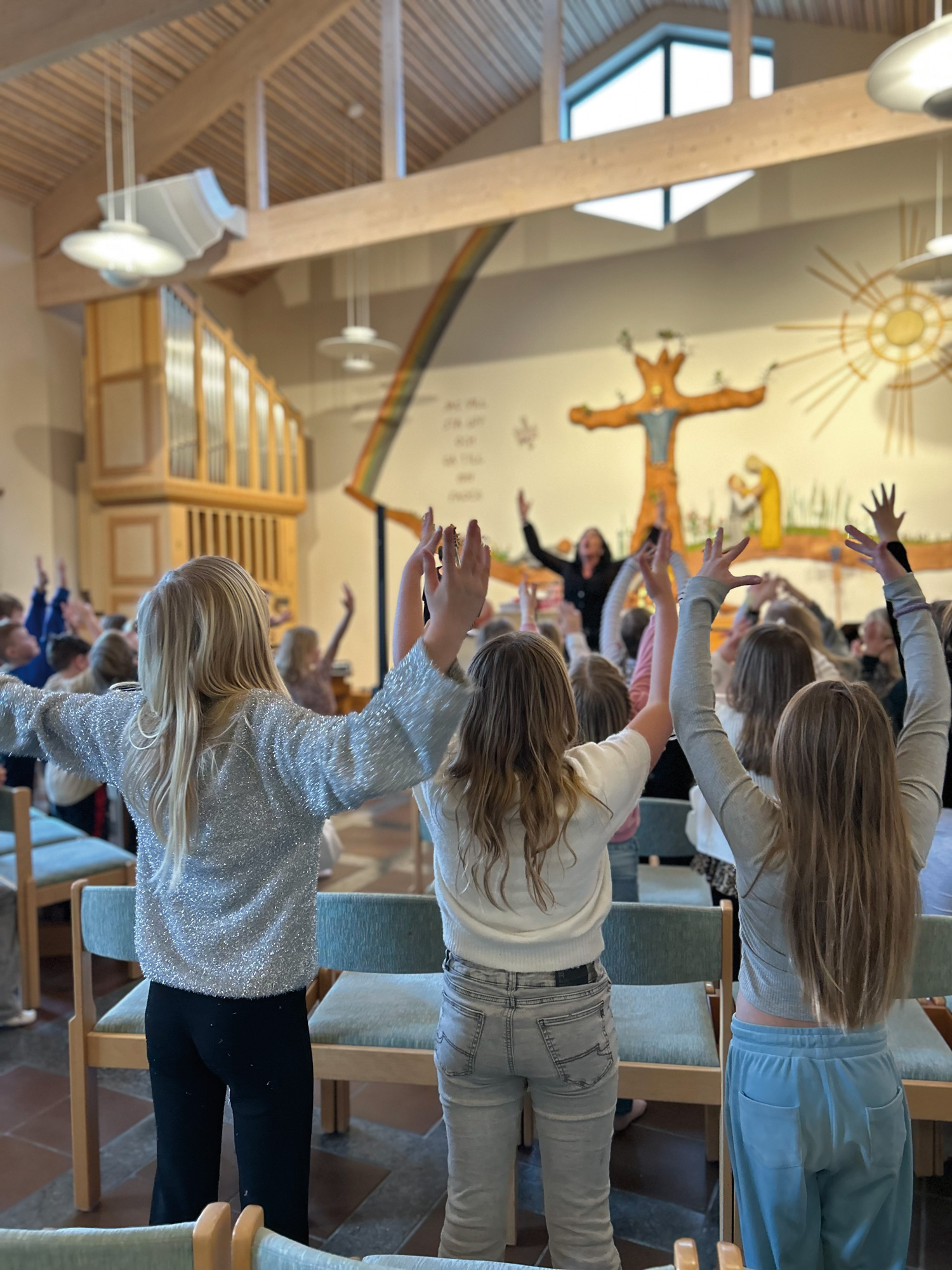 Barn sjunger med lyfta händer på barnkördag på Kyrkans gård