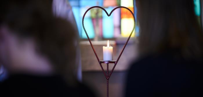 Bild på ett tänt ljus i en ljusbärare, utformat som ett hjärta.