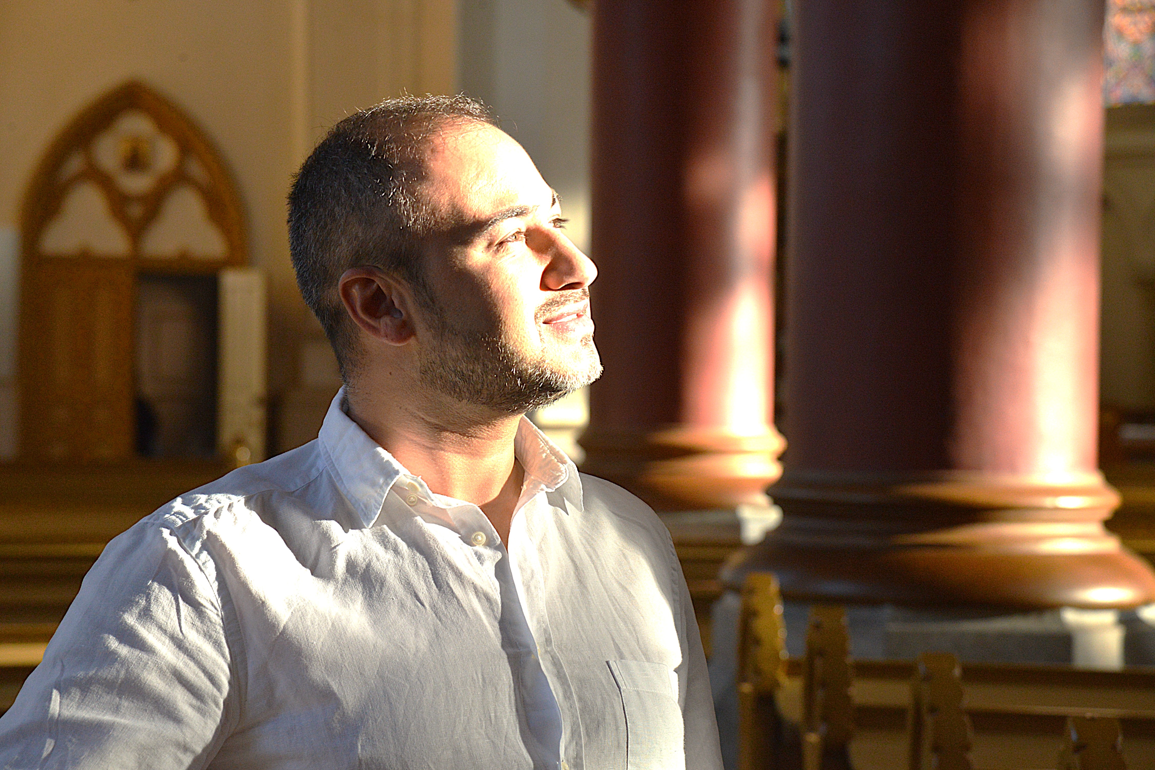 En man i vit skjorta kisar mot solen inne i ett kyrkorum