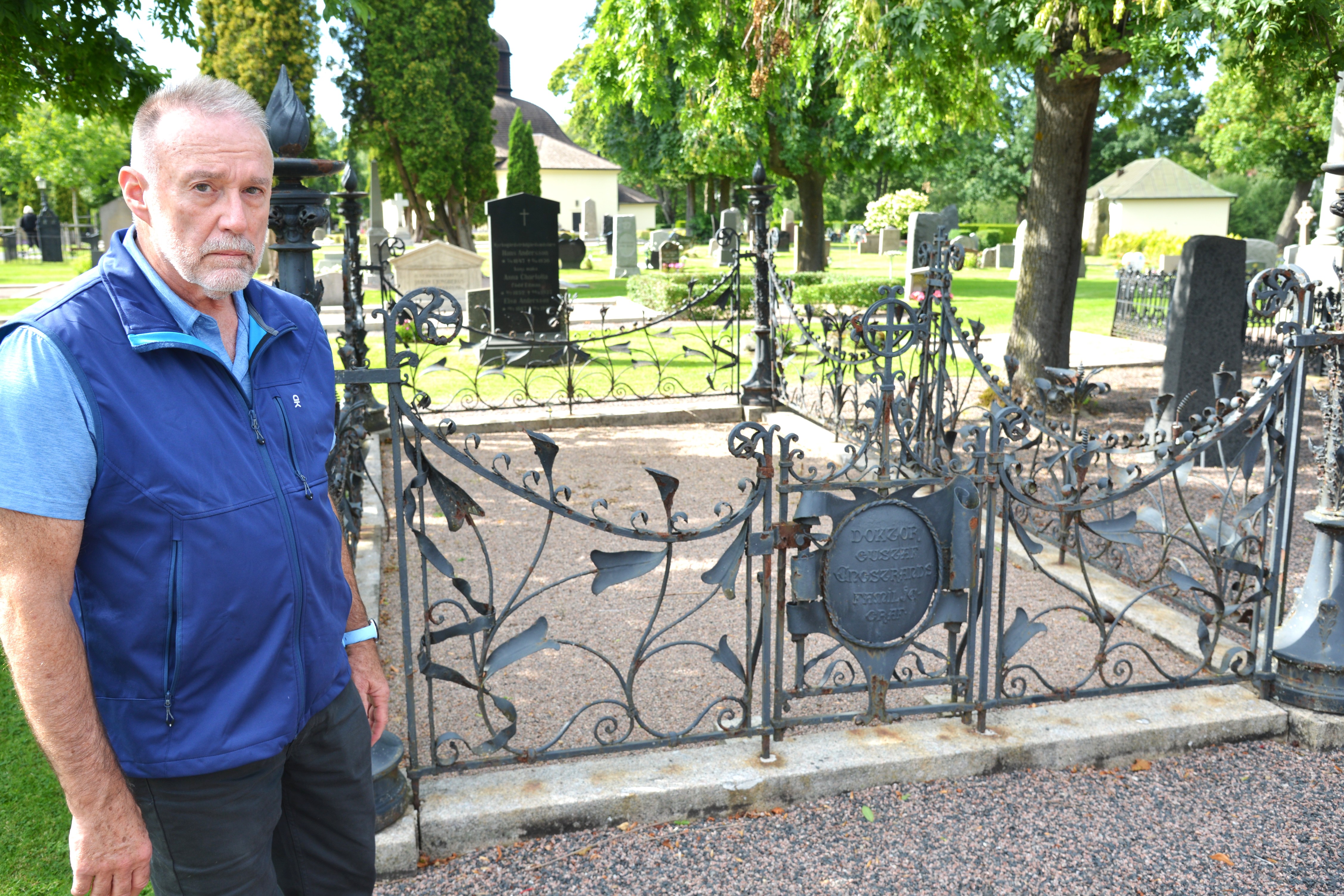 En äldre man står vid ett järnstaket på en kyrkogård