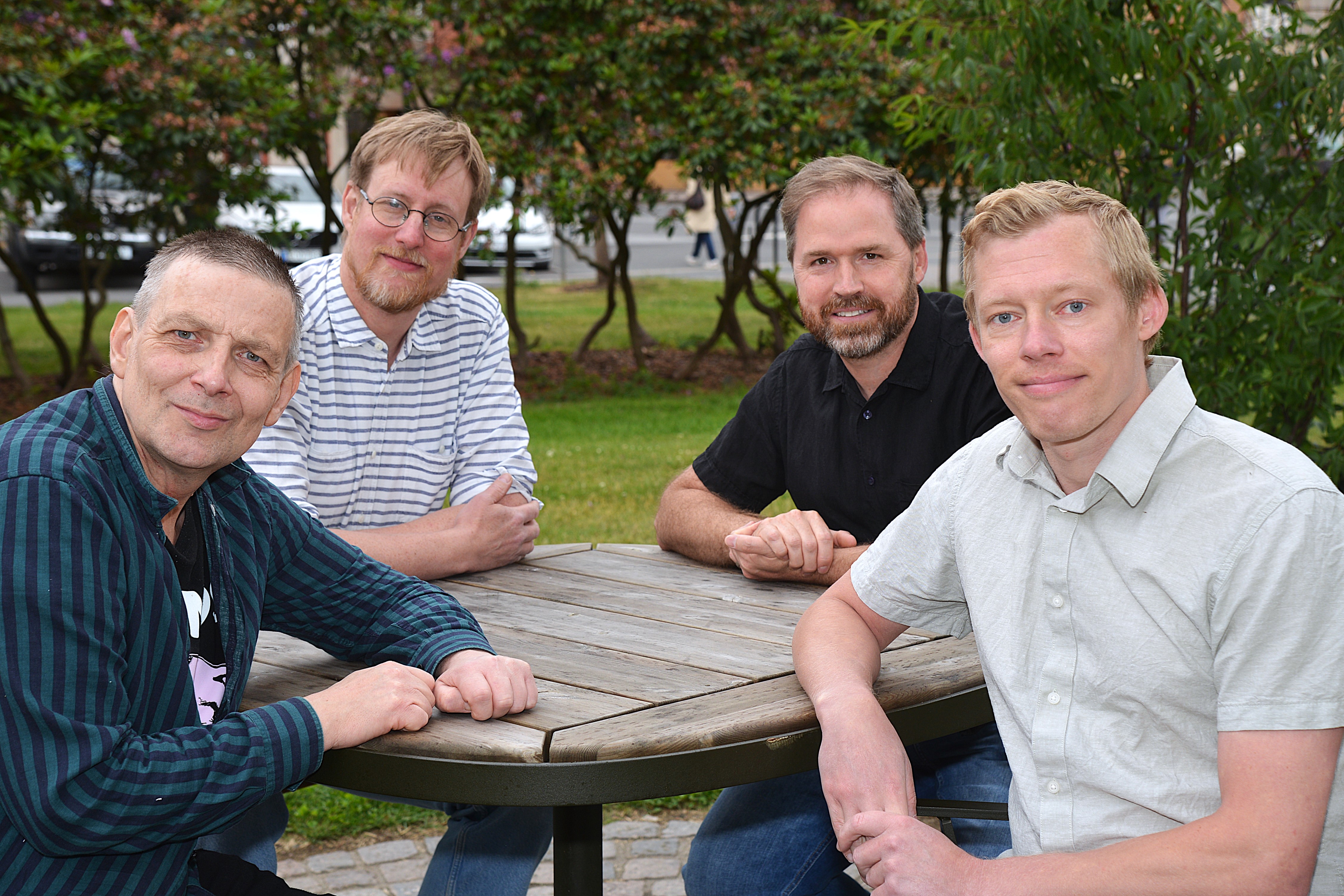 Fyra män sitter utomhus runt ett bord.